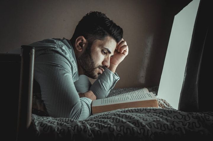 Well groomed bearded fit young man reading a book on his bed